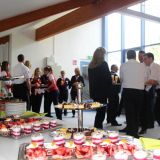 Ein Buffet mit kleinen gefüllten süßen Gläsern und Kuchen. Gäste stehen dahinter.