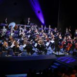 Auf der Bühne spielt ein Orchester von vorne fotografiert. Der Dirigent steht davor.