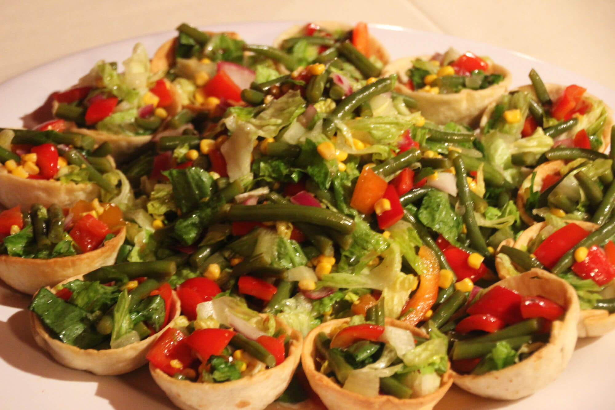Ein Teller mit kleinen gefüllten Teigschalen. Diese sind mit Salat, Mais, Bohnen und Paprika gefüllt.