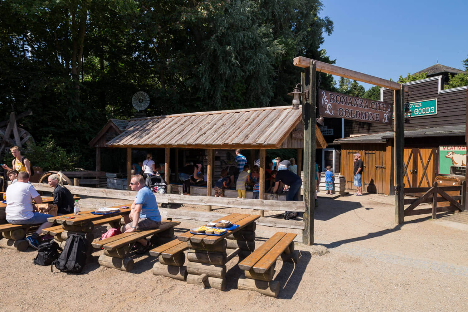 Die Bänke in der Nähe vom Kiosk Joes’s Grill N BBQ und vom Goldwaschen. Dort sitzen Gäste und essen.