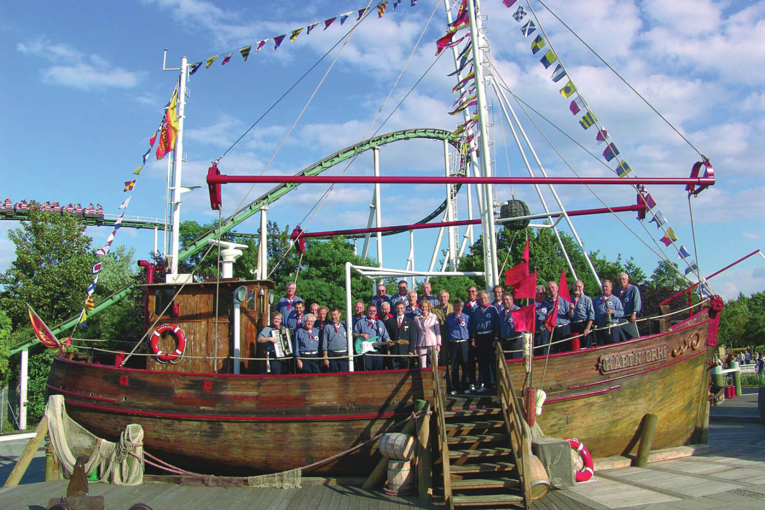 Ein Gruppenfoto auf dem Schiff Käpt’n Orki. Sie lächeln in die kamera. Dahinter fährt der Zug der Nessie.