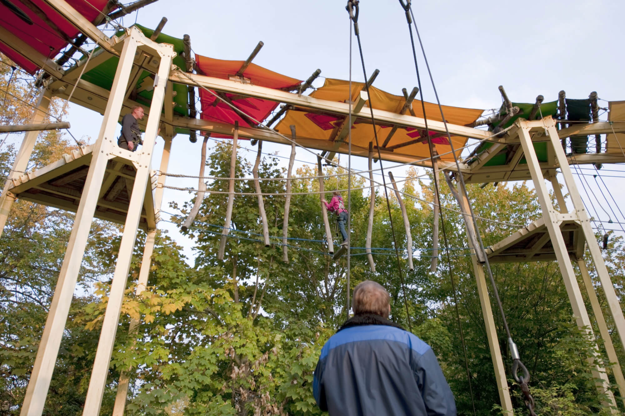 Ein Mann schaut zwei mutigen Kletterern mit Klettergurten im Hochseilgarten Navajo Trail zu.